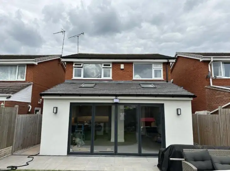 Newly built rear extension in Coventry featuring modern white render, grey aluminium bi-fold doors and twin rooflights on a tiled roof.