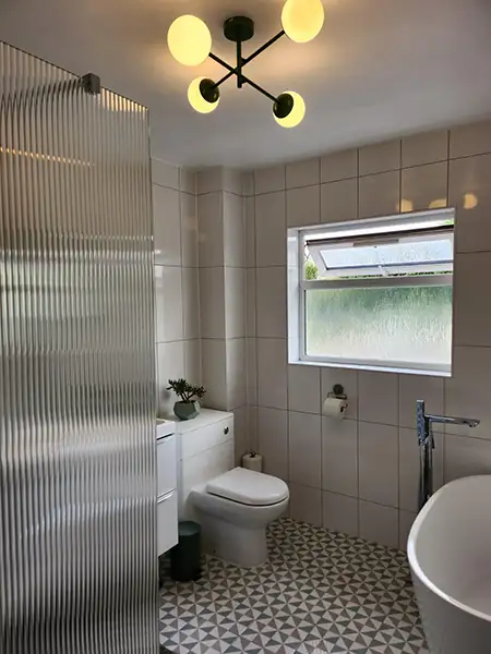 Fully renovated bathroom in Bedworth featuring a modern walk-in shower, patterned floor tiles, white wall tiles and contemporary lighting.